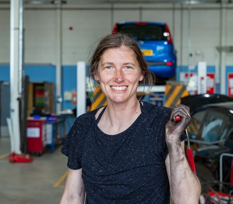 Mecánica sonriendo en un taller con una llave en la mano